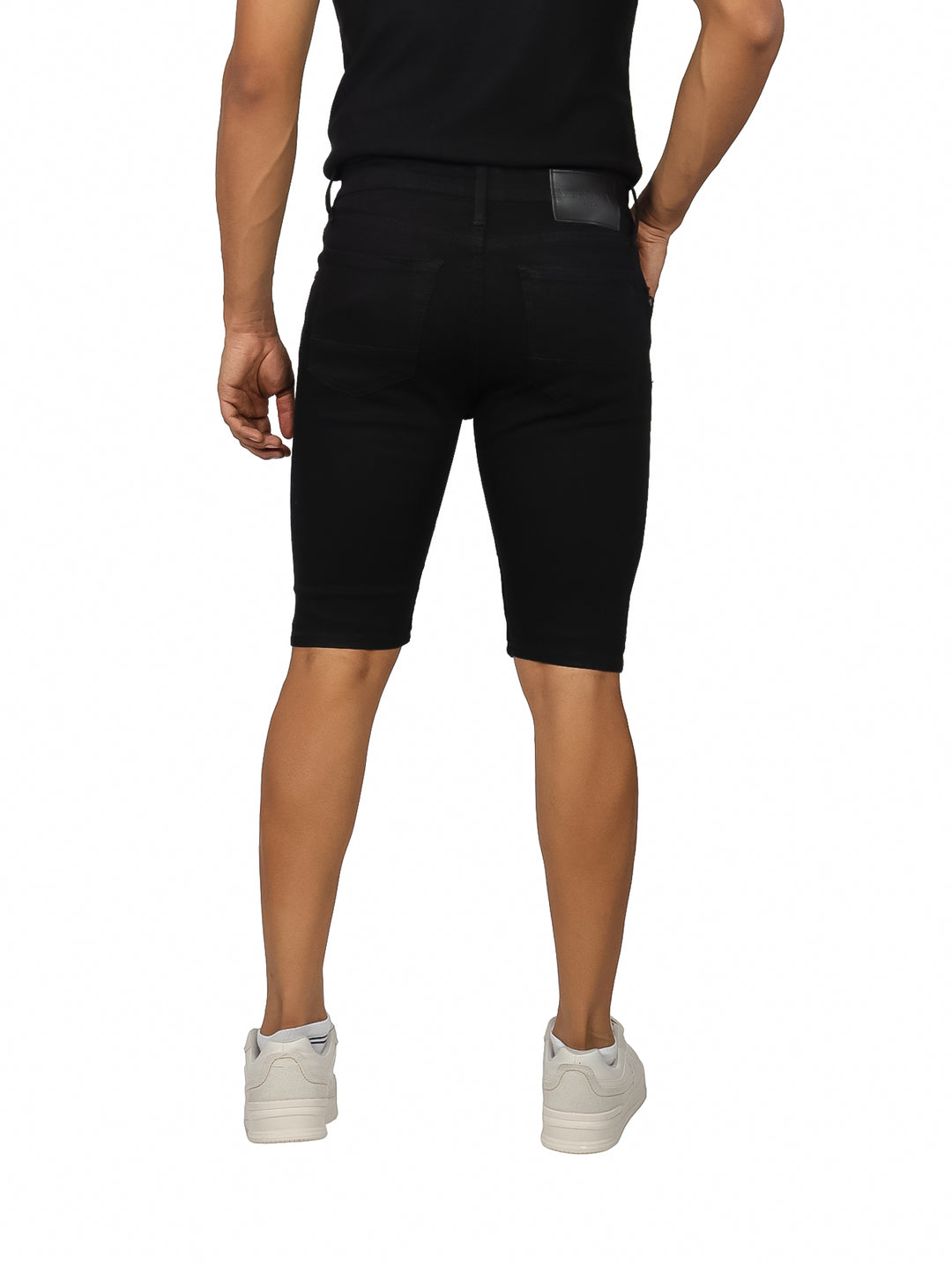 Hombre vistiendo bermuda de mezclilla color negro con detalles rotos en las piernas.