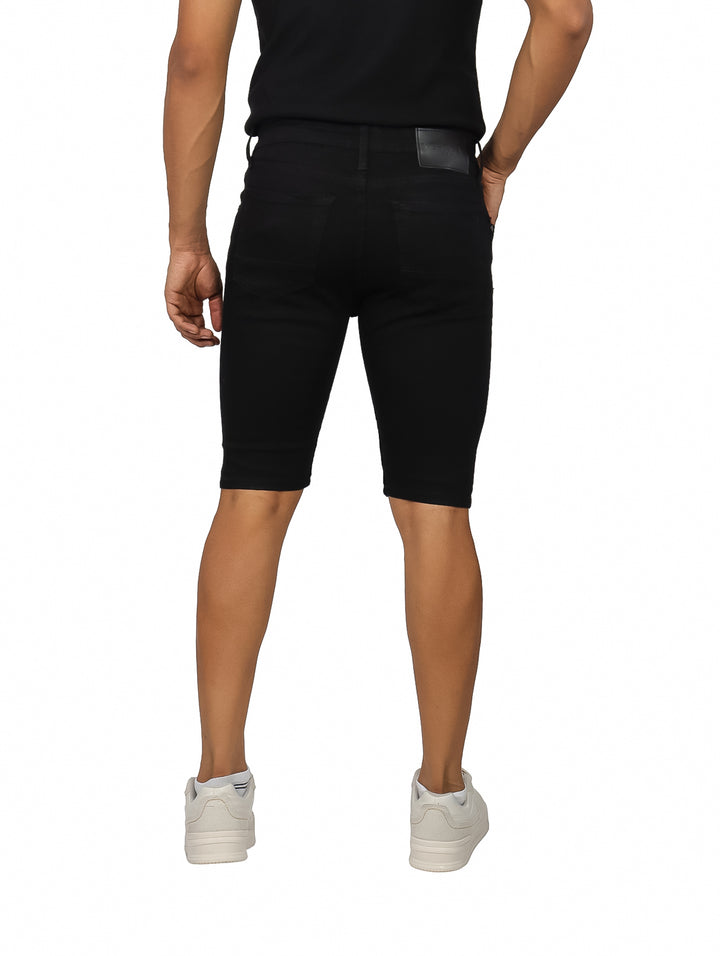 Hombre vistiendo bermuda de mezclilla color negro con detalles rotos en las piernas.