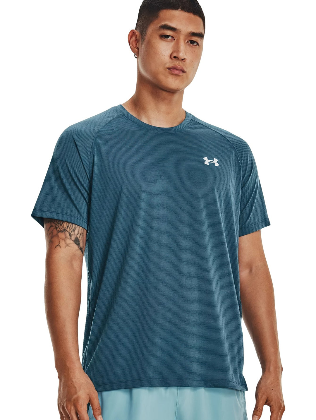 Hombre usando camiseta deportiva Under Armour de color azul con logo blanco en el pecho.