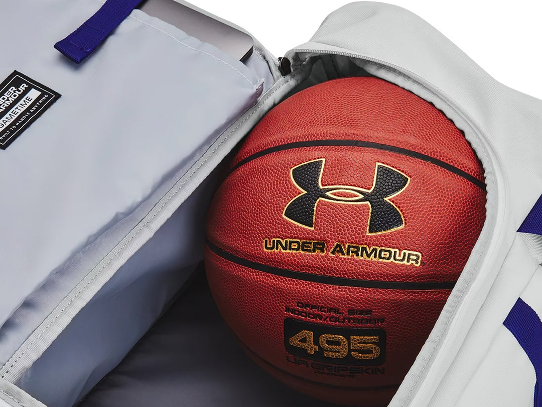 Maleta deportiva Under Armour color gris con detalles en azul, incluye asas y correa para el hombro.