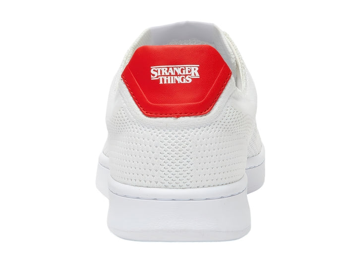 Tenis blancos Lacoste de tela con detalle rojo en el talón y logotipo bordado en el costado.