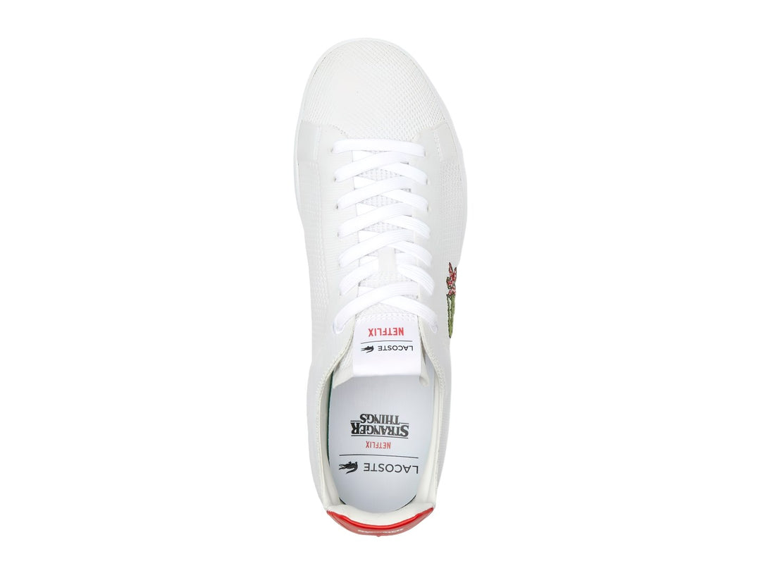 Tenis blancos Lacoste de tela con detalle rojo en el talón y logotipo bordado en el costado.