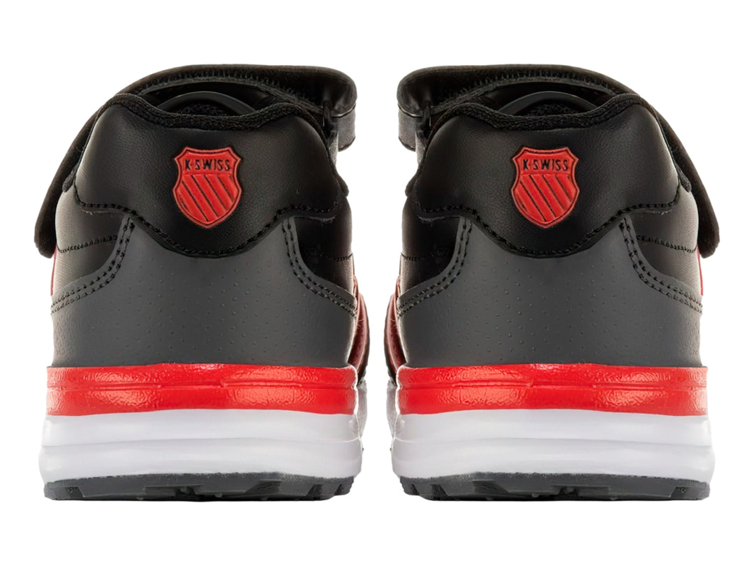Tenis K-SWISS color negro con franjas rojas laterales, suela blanca y cierre de velcro para niño.