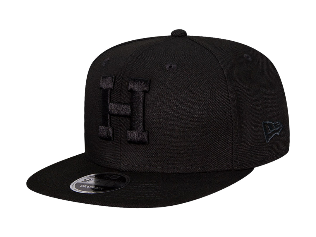 Gorra de béisbol New Era color negro con visera plana y letra H bordada en relieve en el frente.
