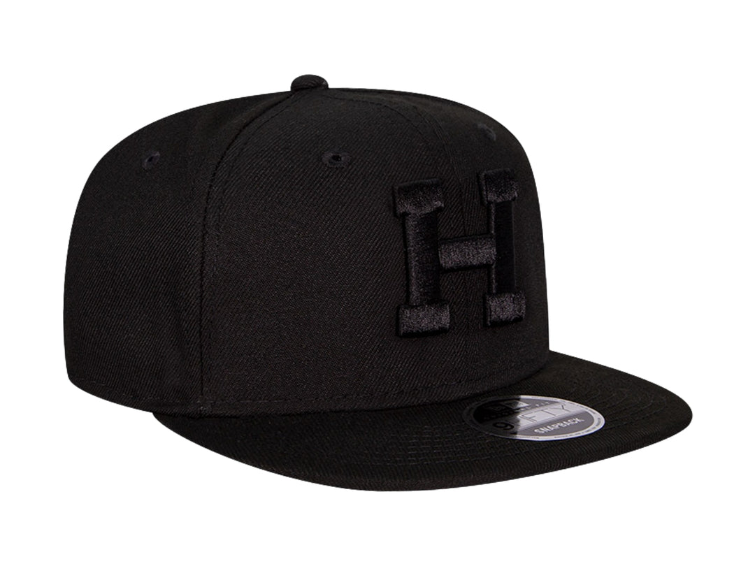 Gorra de béisbol New Era color negro con visera plana y letra H bordada en relieve en el frente.