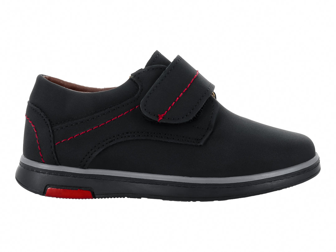 Zapato infantil color negro con costuras rojas y cierre de velcro.