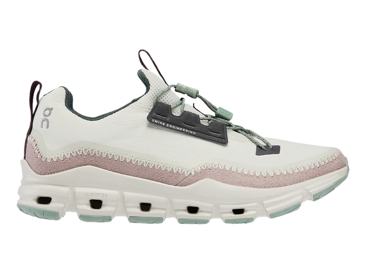 Tenis deportivos On Cloud color gris claro con banda morada y suela blanca con detalles verdes.