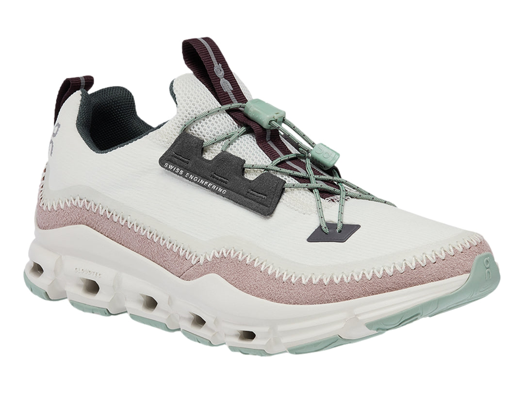 Tenis deportivos On Cloud color gris claro con banda morada y suela blanca con detalles verdes.