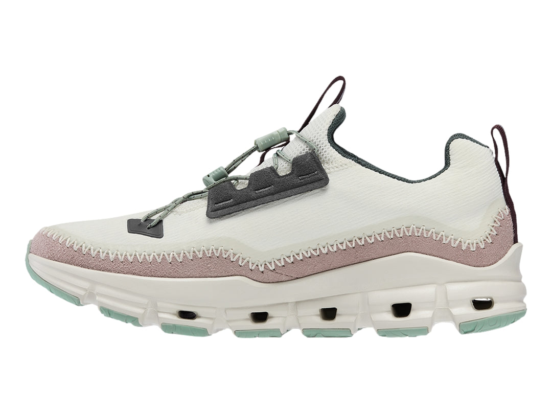 Tenis deportivos On Cloud color gris claro con banda morada y suela blanca con detalles verdes.