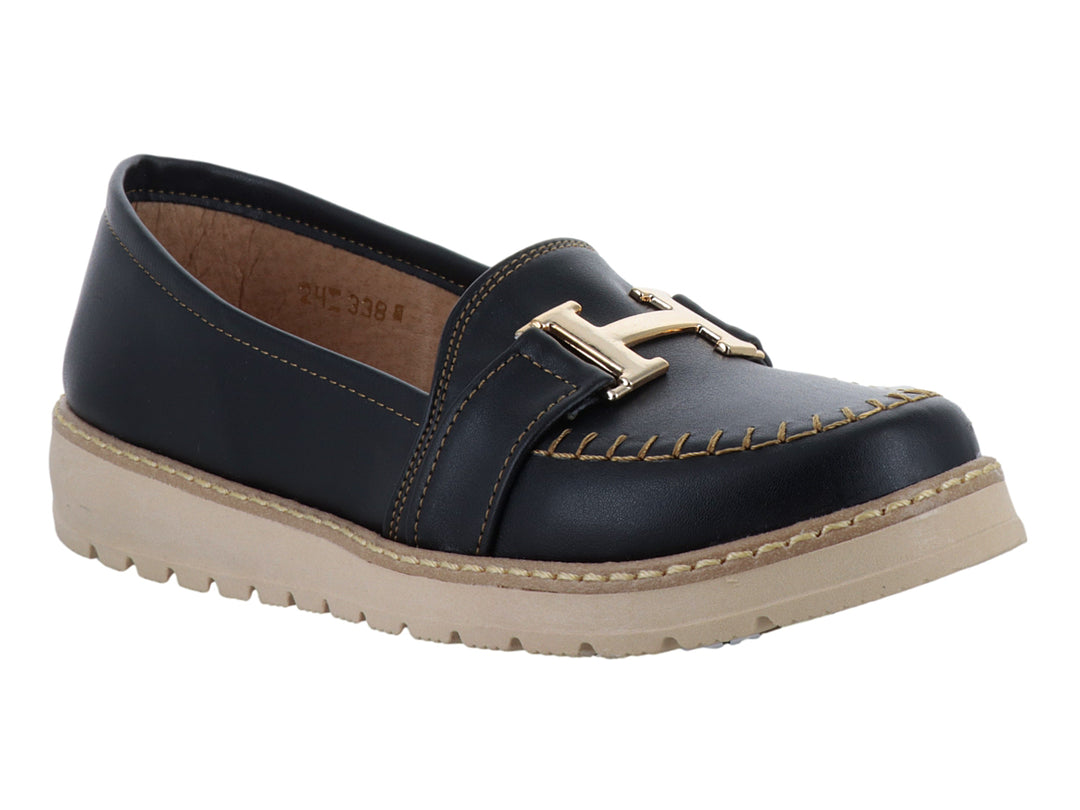 Zapato tipo mocasín color negro con suela gruesa beige y detalle metálico dorado en la parte superior.