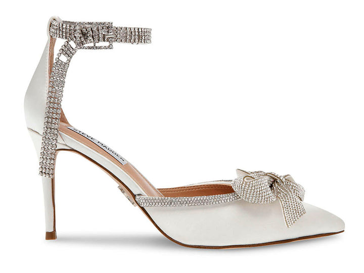 Zapato de tacón Steve Madden en color marfil satinado con detalles de cristales y un moño decorativo en la punta.