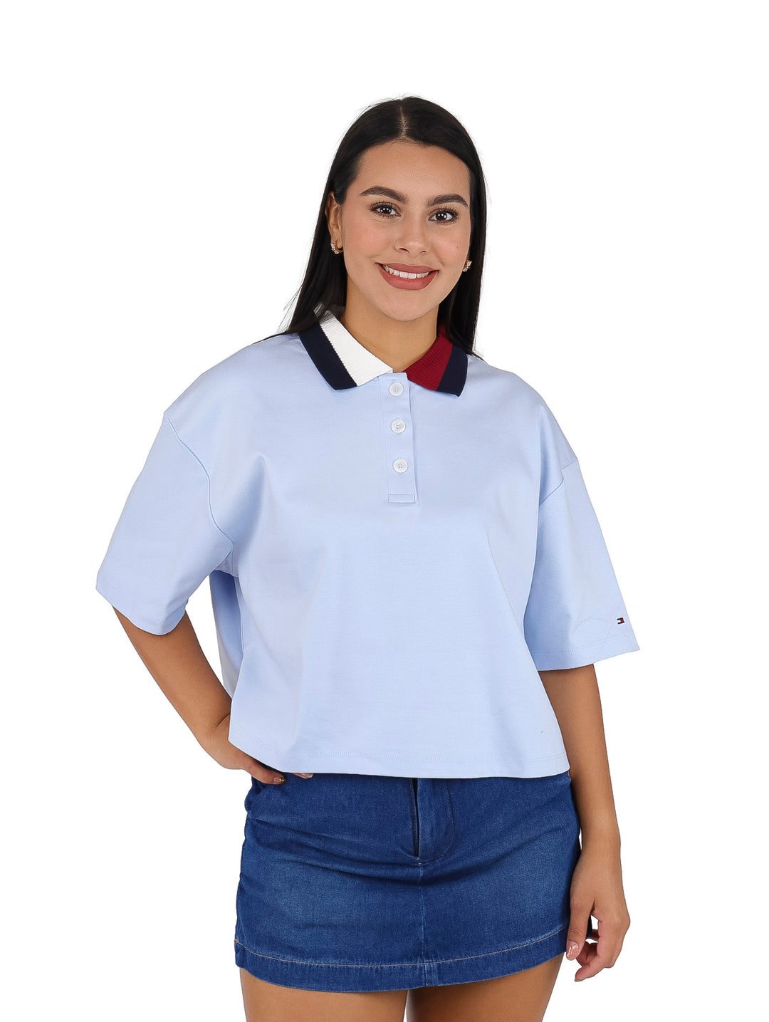 Mujer vistiendo polo crop color azul claro de Tommy Hilfiger con cuello tricolor y falda denim.