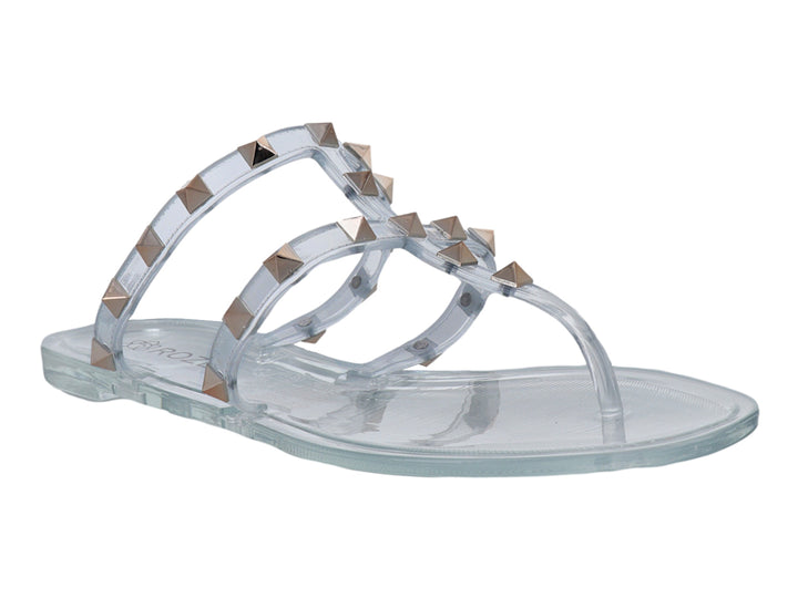 Sandalia plana transparente para niña con tiras decoradas con tachuelas doradas.