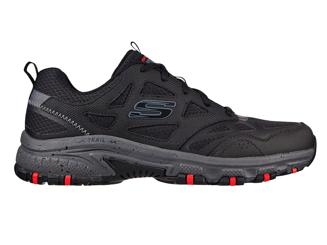 Zapato deportivo Skechers en color negro y gris con detalles rojos en la suela, ideal para actividades de trail.