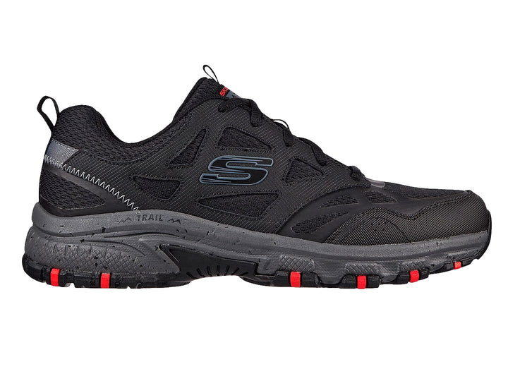 Zapato deportivo Skechers en color negro y gris con detalles rojos en la suela, ideal para actividades de trail.