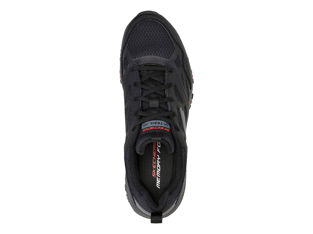 Zapato deportivo Skechers en color negro y gris con detalles rojos en la suela, ideal para actividades de trail.