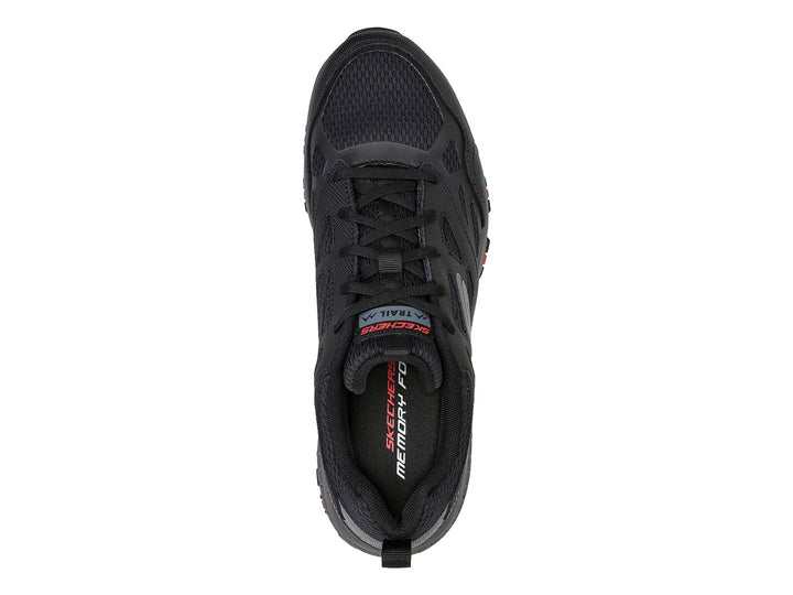 Zapato deportivo Skechers en color negro y gris con detalles rojos en la suela, ideal para actividades de trail.