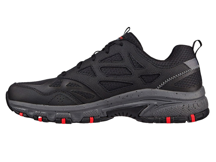 Zapato deportivo Skechers en color negro y gris con detalles rojos en la suela, ideal para actividades de trail.