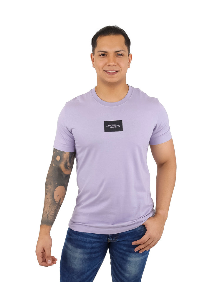 Hombre vistiendo una camiseta de manga corta color morado claro con un pequeño logo central negro de Calvin Klein.