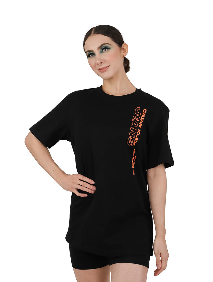 Mujer vistiendo una camiseta negra de manga corta con logotipo naranja de Calvin Klein Jeans.