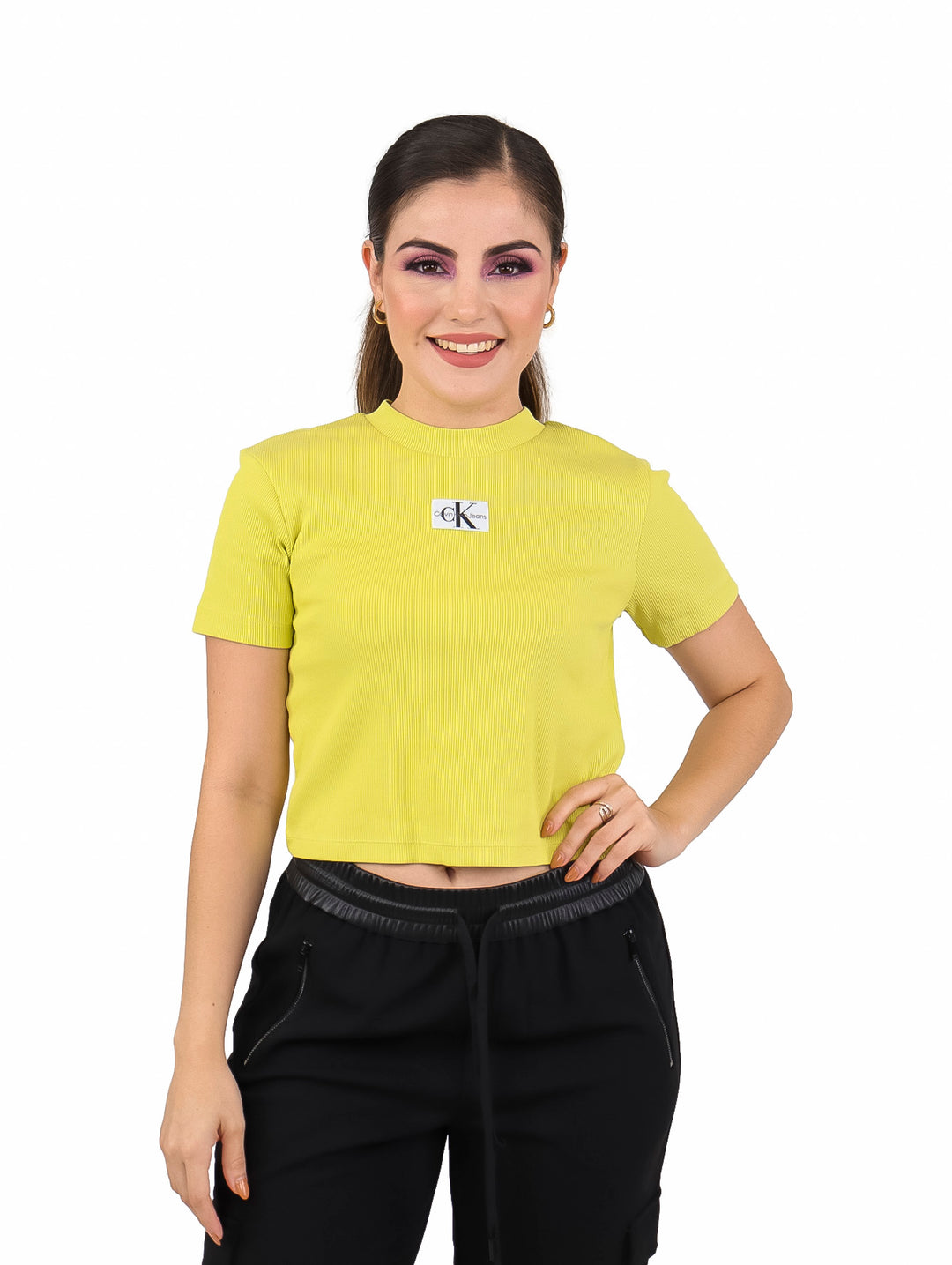 Mujer con camiseta corta de manga corta color oro con textura acanalada y logo frontal.