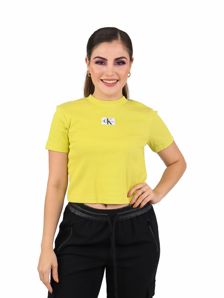 Mujer con camiseta corta de manga corta color oro con textura acanalada y logo frontal.