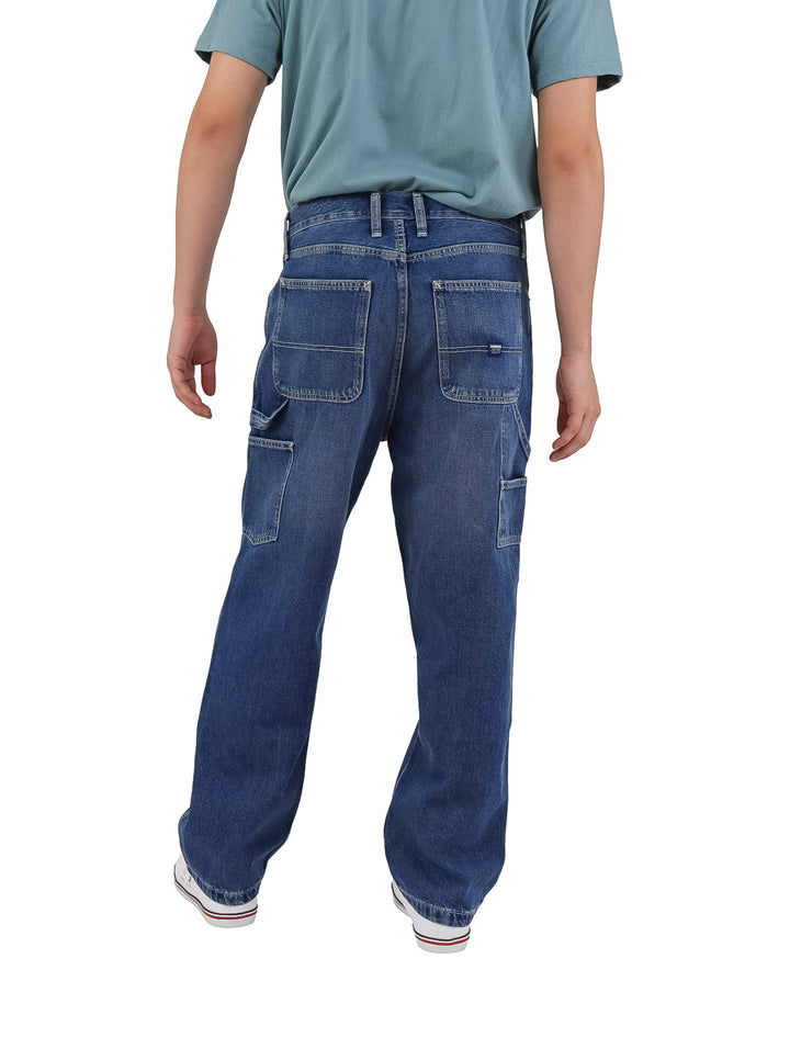 Hombre vistiendo pantalones de mezclilla azules estilo carpenter de corte recto y calzado blanco.