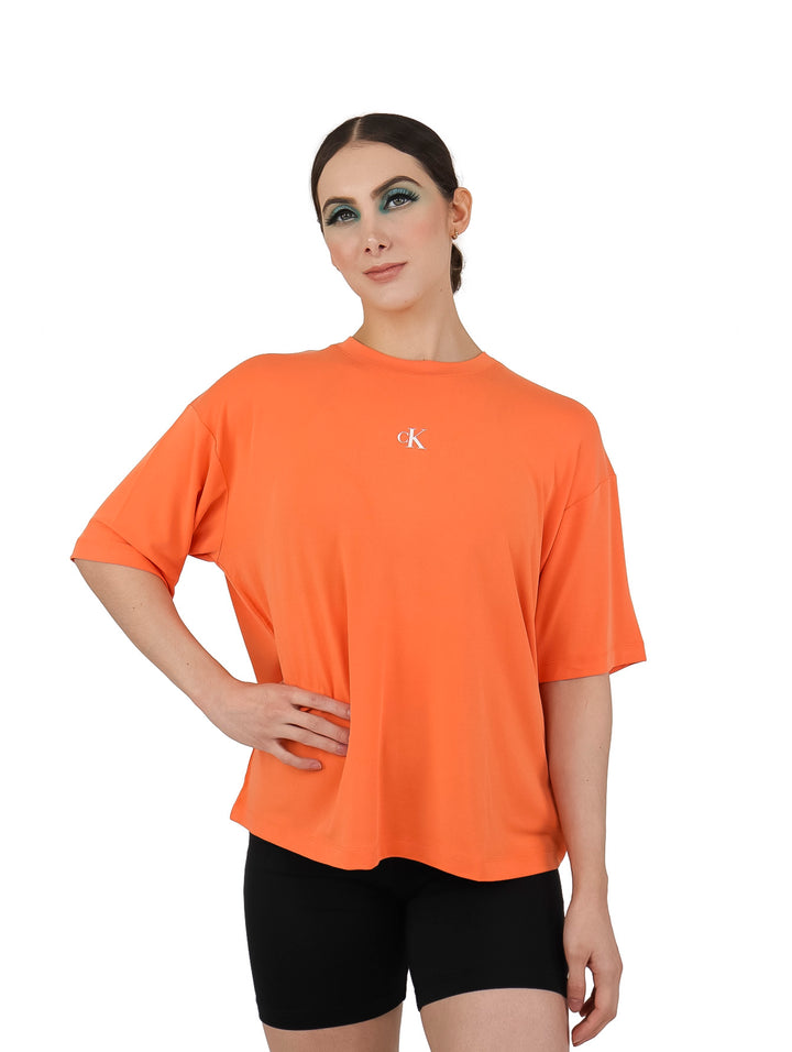 Mujer vistiendo una camiseta naranja holgada de Calvin Klein y shorts negros sobre fondo blanco.