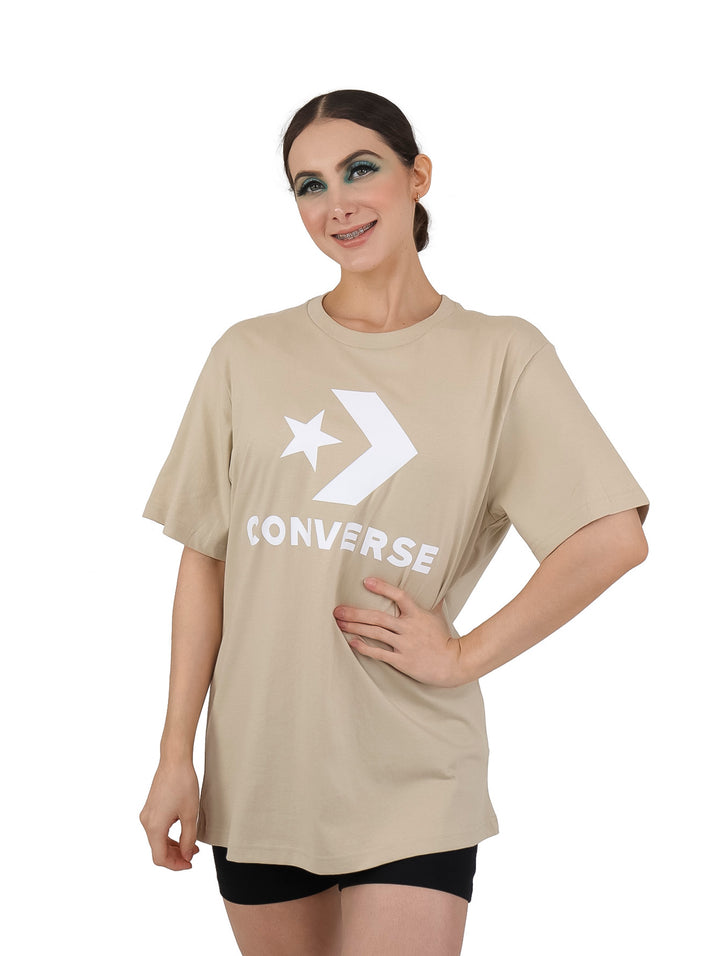 Mujer vistiendo playera beige de manga corta con logotipo de Converse en color blanco.