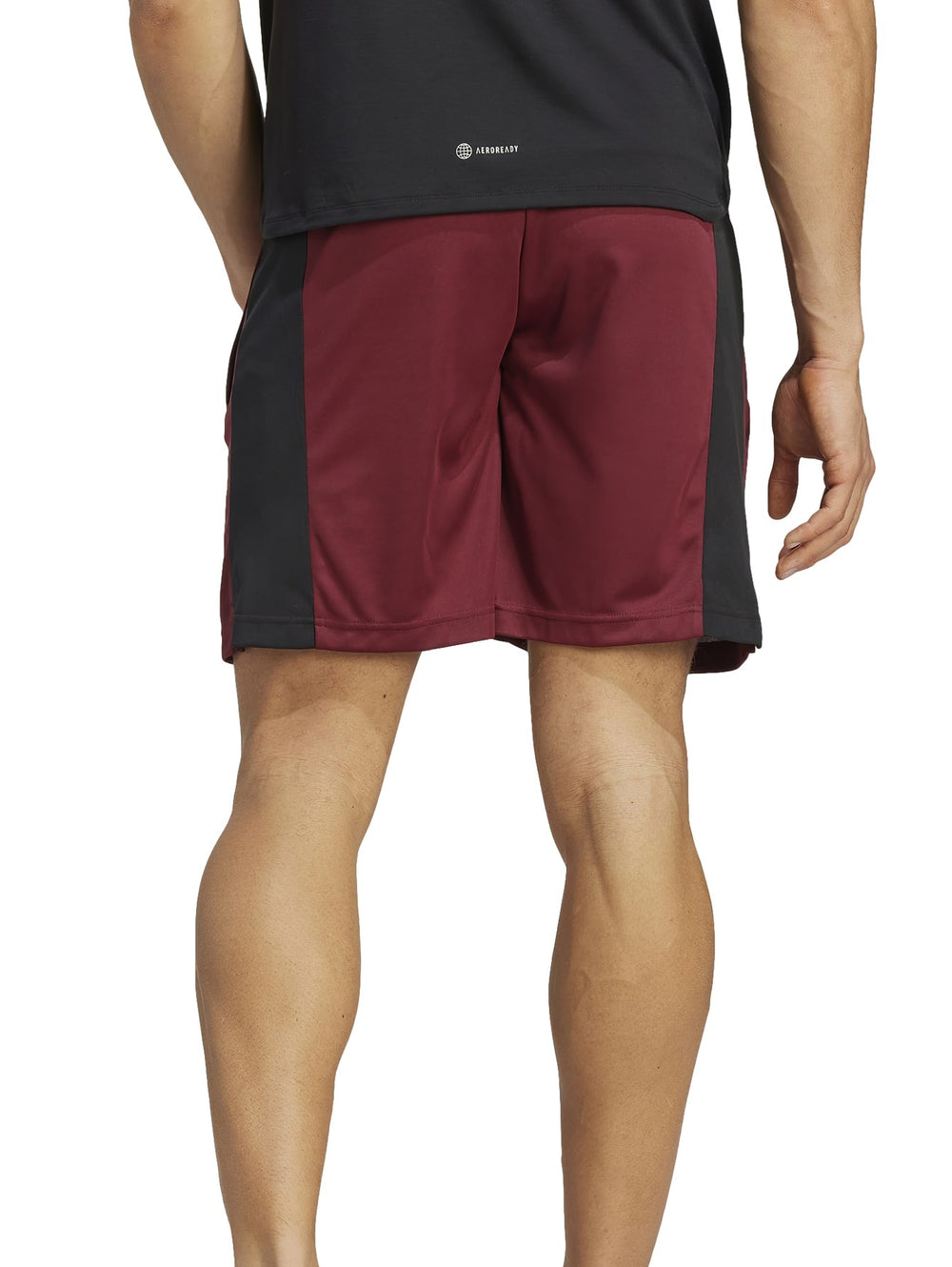 Hombre vistiendo shorts deportivos Adidas color guinda con paneles laterales negros.