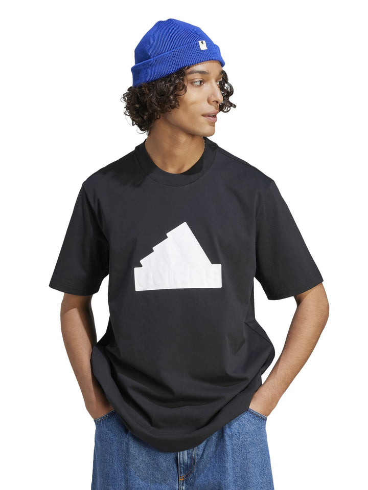 Hombre usando camiseta negra Adidas con gráfico blanco, gorro azul y pantalones mezclilla.