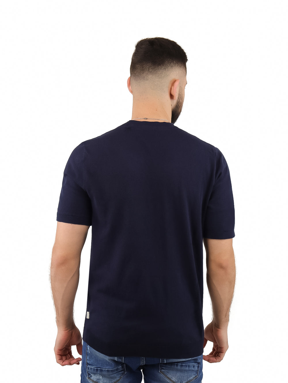 Hombre vistiendo una camiseta de manga corta color azul marino con cuello redondo y jeans azules.