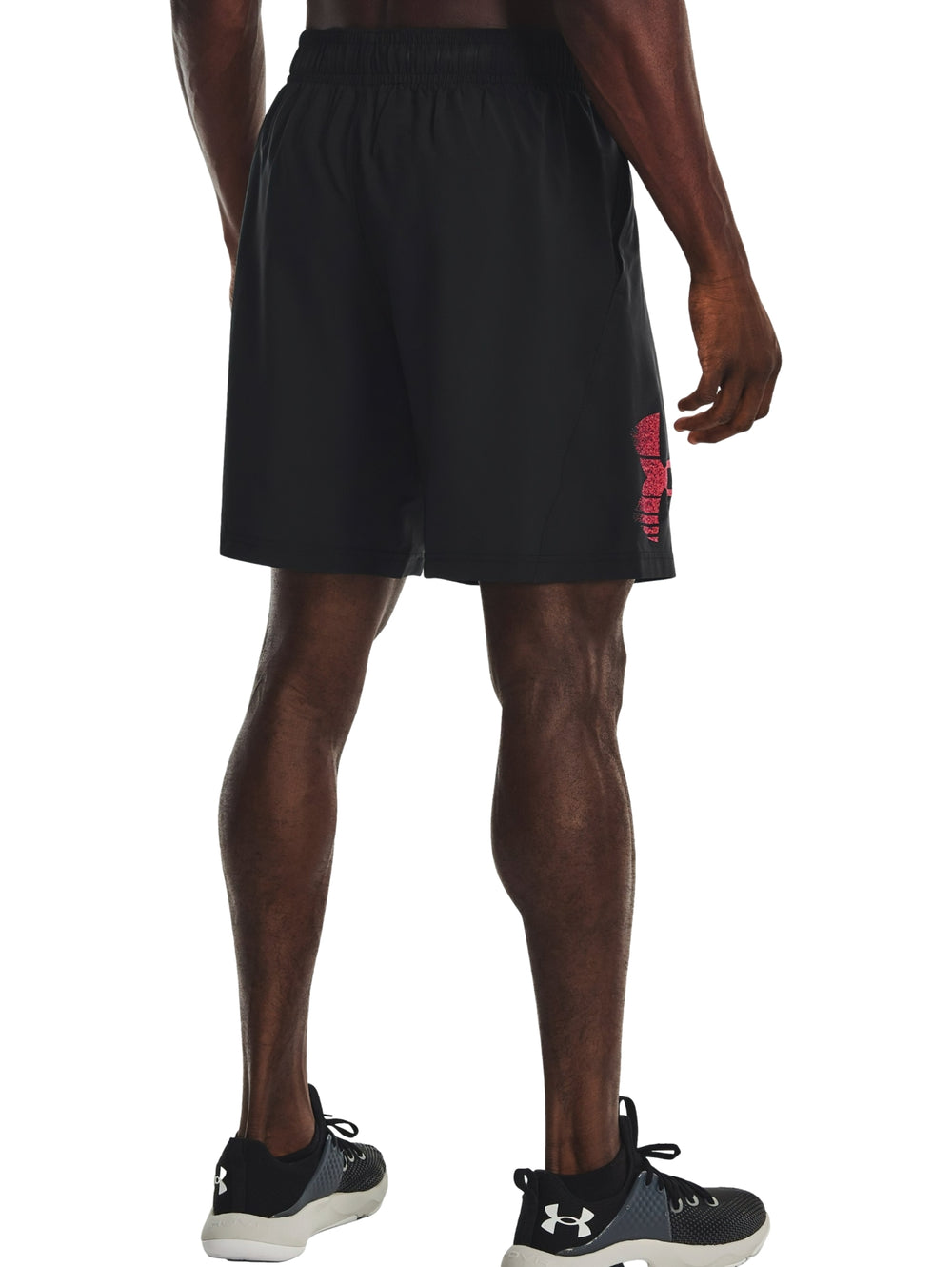 Hombre vistiendo shorts deportivos negros de Under Armour con logotipo gráfico rojo.