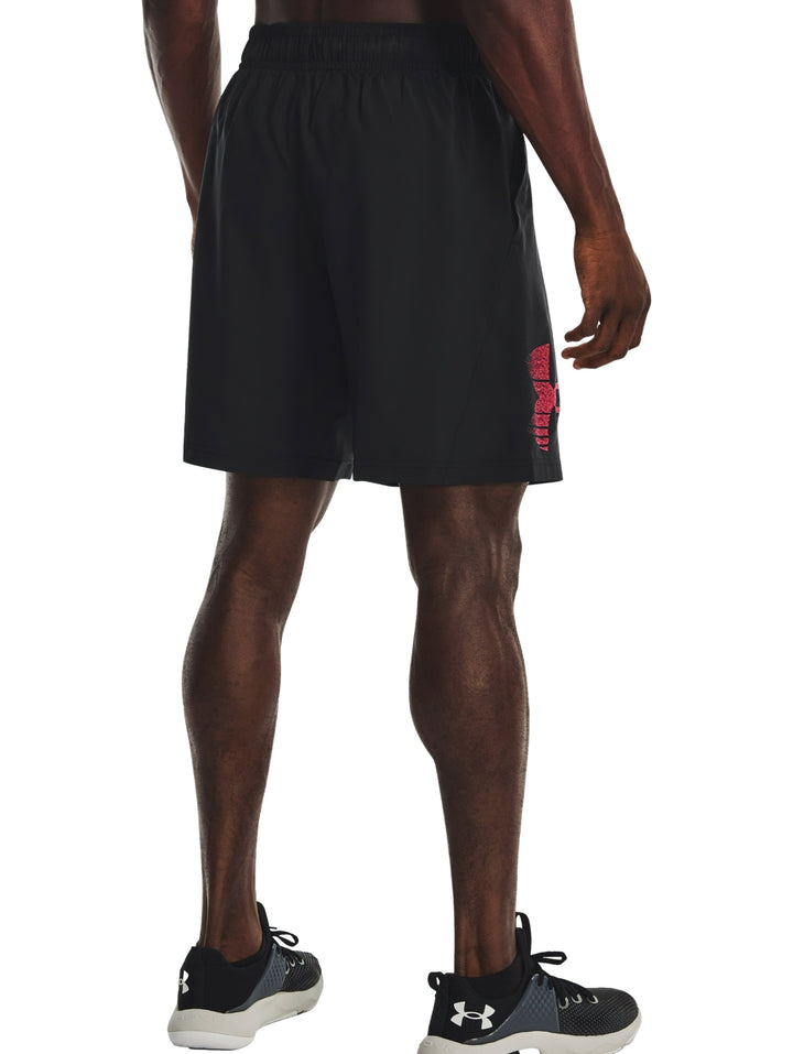 Hombre vistiendo shorts deportivos negros de Under Armour con logotipo gráfico rojo.