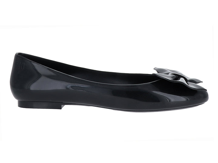 Zapato plano tipo ballerina color negro brillante con detalle de moño en la parte frontal.