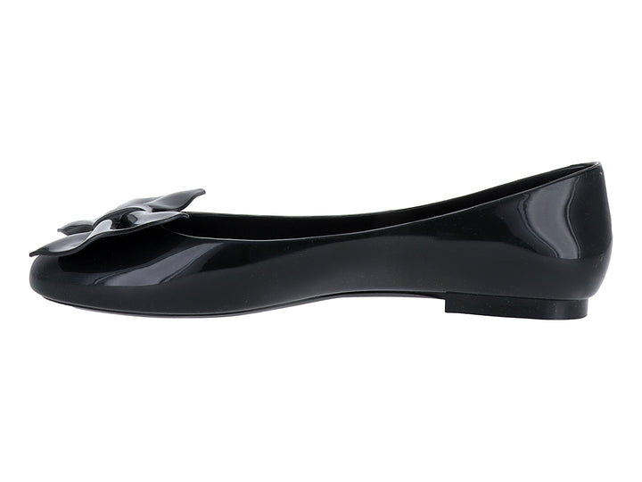 Zapato plano tipo ballerina color negro brillante con detalle de moño en la parte frontal.