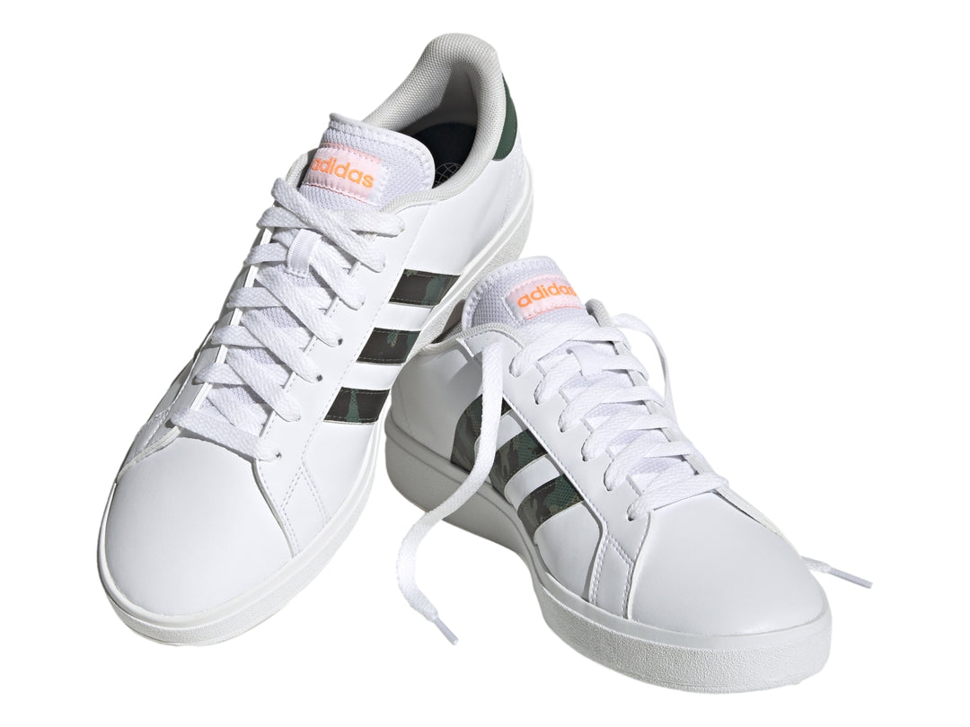 Tenis Adidas blancos con franjas laterales en patrón de camuflaje y detalles en naranja.