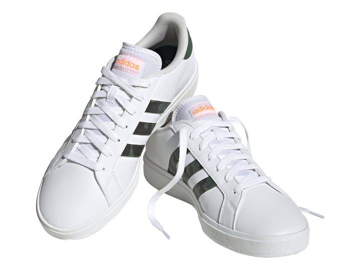 Tenis Adidas blancos con franjas laterales en patrón de camuflaje y detalles en naranja.