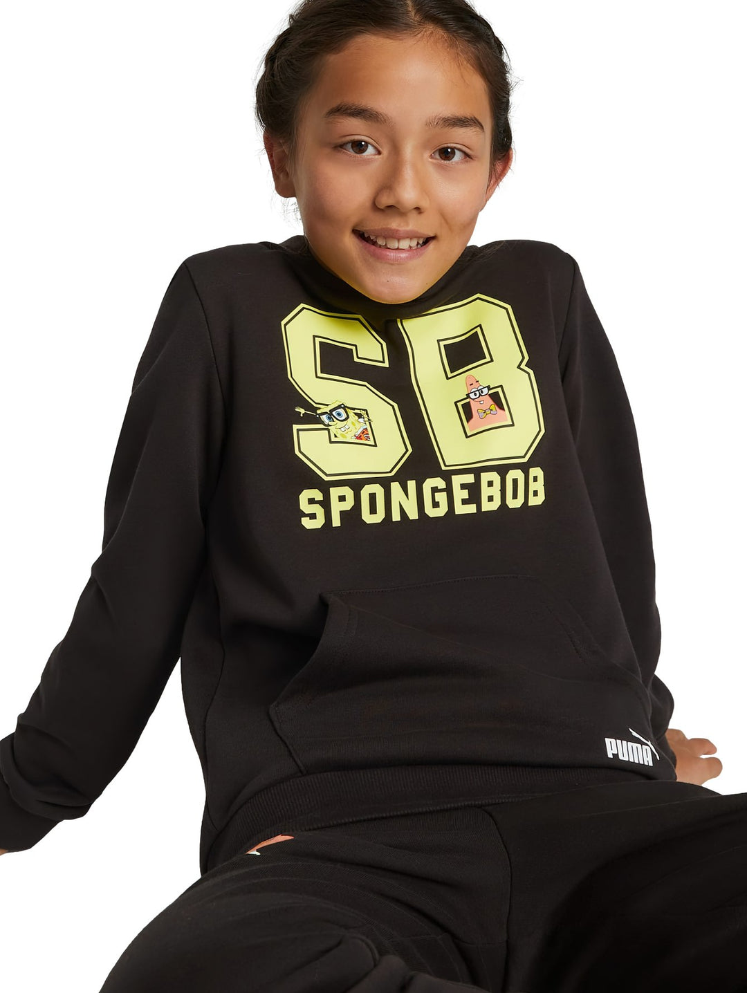 Sudadera negra PUMA x SpongeBob con gráfico amarillo frontal y bolsillo canguro, usada por una niña.
