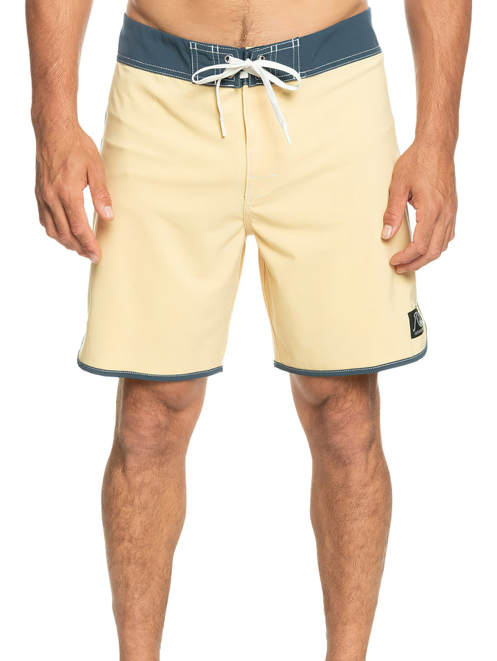 Hombre vistiendo traje de baño corto color beige con cintura y bordes en azul oscuro.