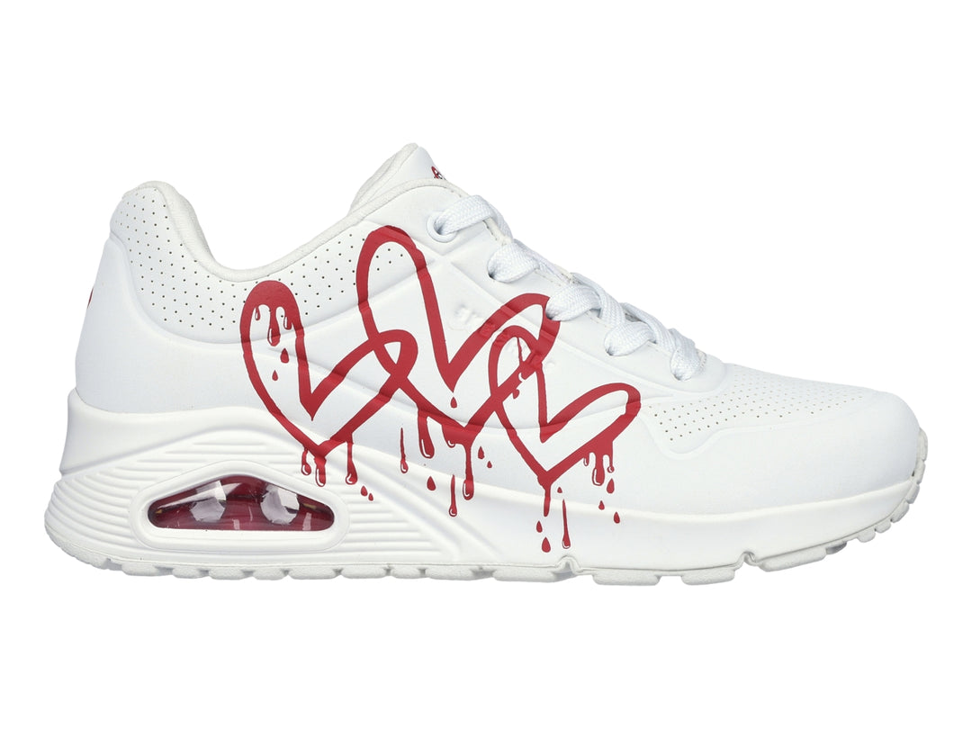 Tenis Skechers blancos con diseño de corazones rojos en efecto goteo y suela amortiguada.