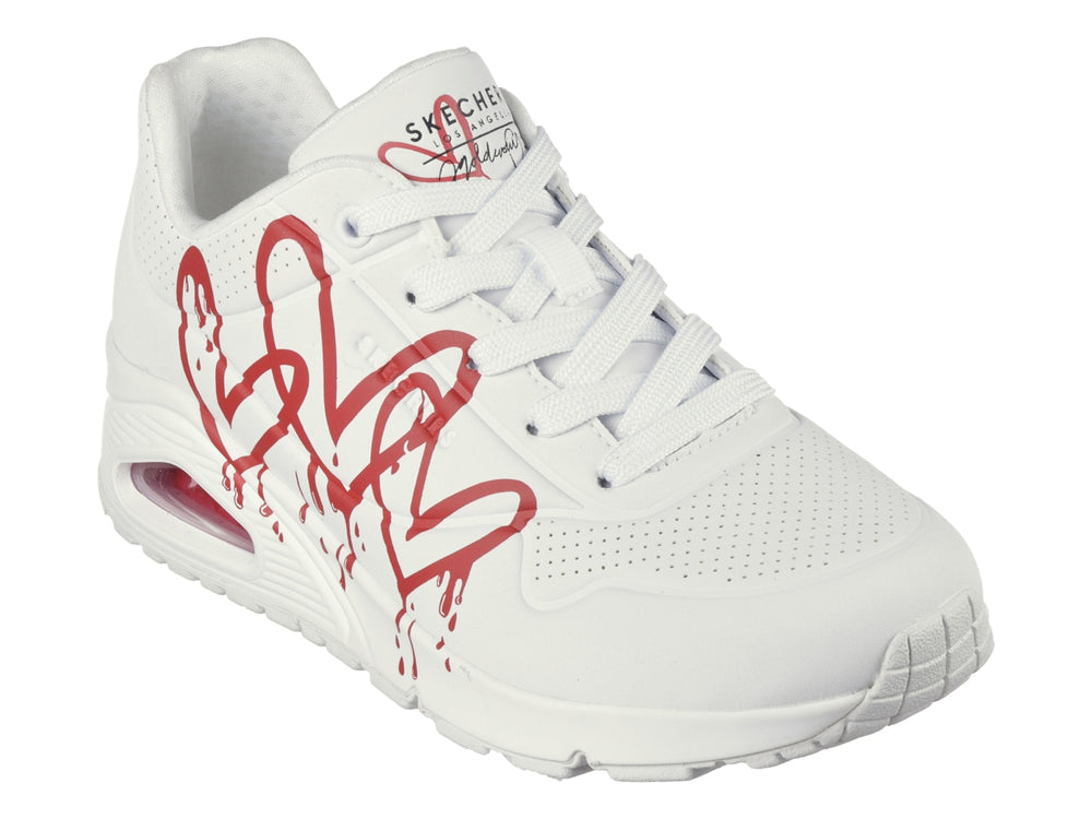 Tenis Skechers blancos con diseño de corazones rojos en efecto goteo y suela amortiguada.