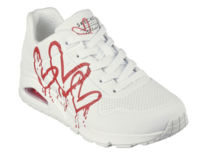 Tenis Skechers blancos con diseño de corazones rojos en efecto goteo y suela amortiguada.