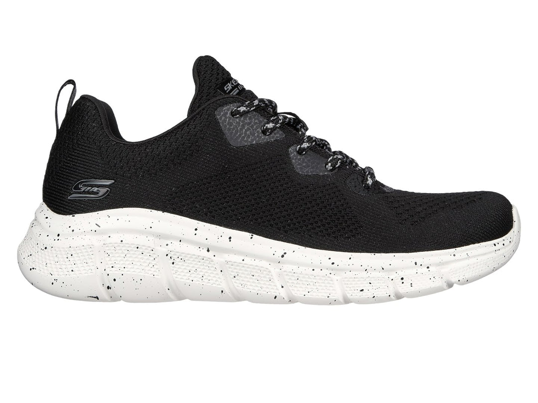 Tenis Skechers negros con suela blanca moteada y tejido transpirable.