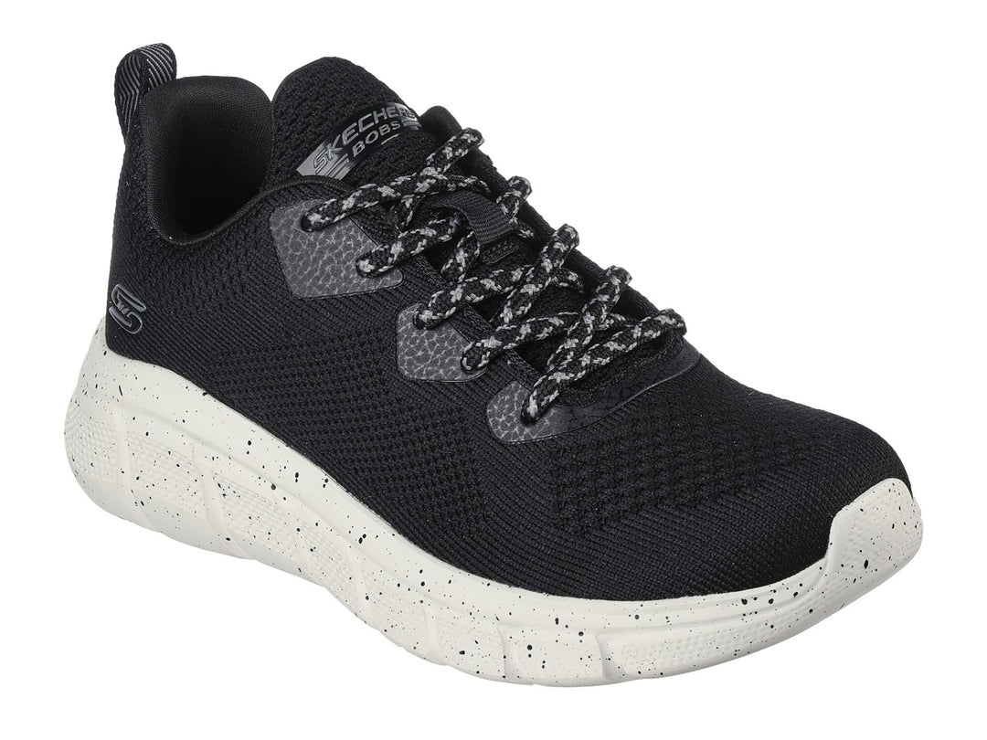 Tenis Skechers negros con suela blanca moteada y tejido transpirable.