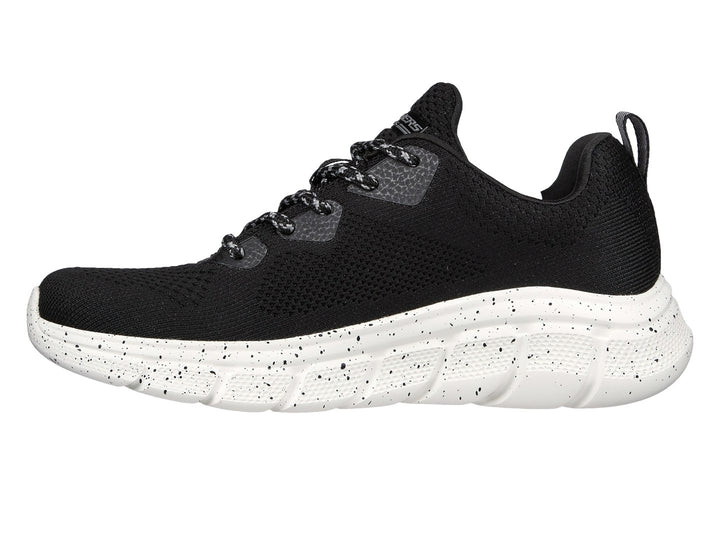 Tenis Skechers negros con suela blanca moteada y tejido transpirable.
