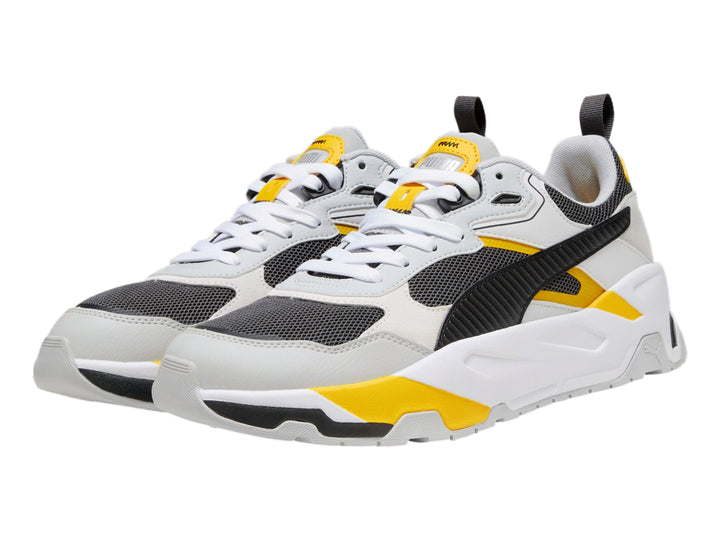 Tenis PUMA Trinity blancos y grises con detalles en amarillo y negro, diseño deportivo de suela gruesa.