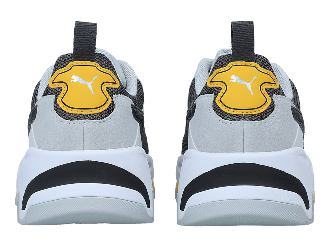 Tenis PUMA Trinity blancos y grises con detalles en amarillo y negro, diseño deportivo de suela gruesa.