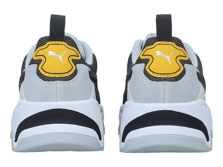 Tenis PUMA Trinity blancos y grises con detalles en amarillo y negro, diseño deportivo de suela gruesa.
