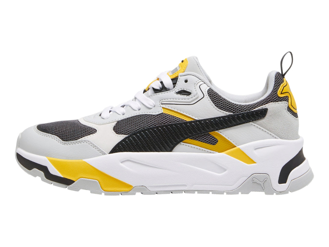 Tenis PUMA Trinity blancos y grises con detalles en amarillo y negro, diseño deportivo de suela gruesa.